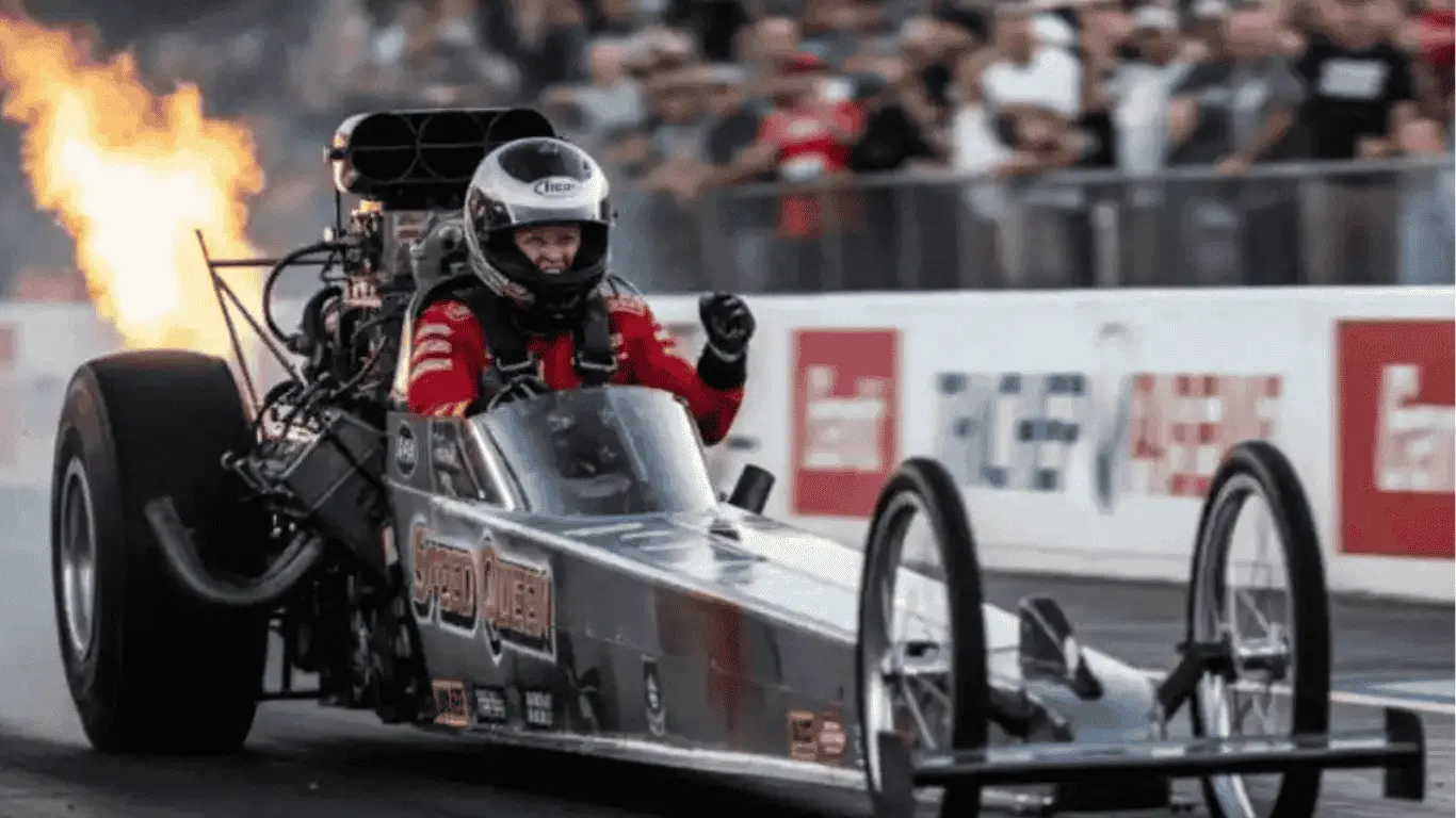 Barbara Roufs-inspired female drag racer driving a high-performance dragster, with flames erupting from the exhaust, celebrating victory at the drag racing track. The 'Speed Queen' car symbolizes breaking barriers in motorsports.